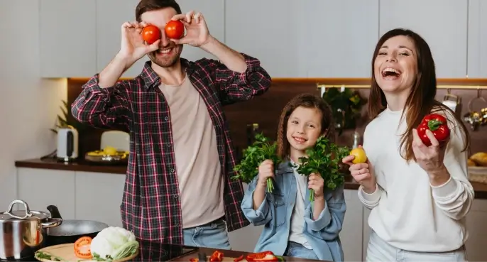 A Smiling family showing off by holding fresh tomatoes, greens, paprika, and lemon in their modern kitchen