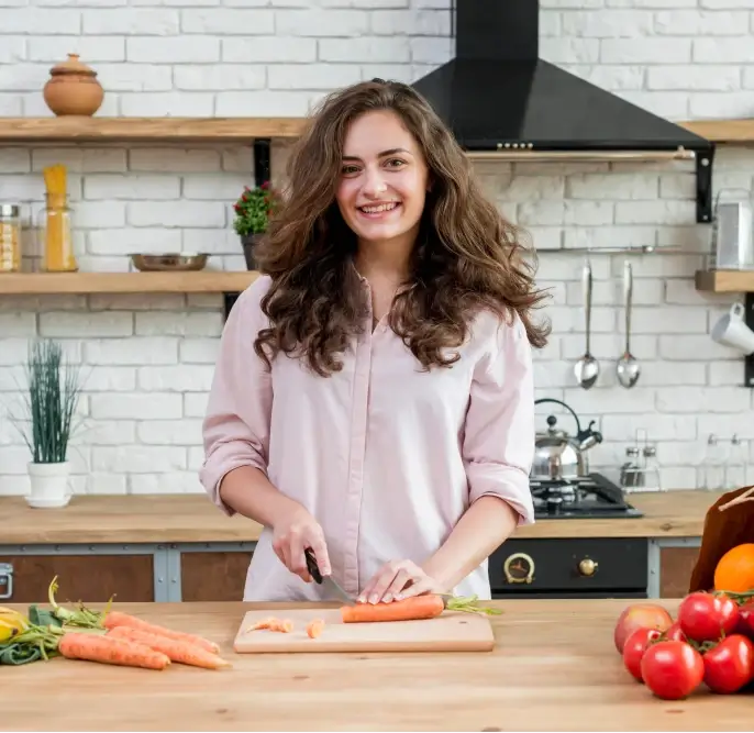 A Smiling woman slicing fresh carrots with knife in a cozy kitchen