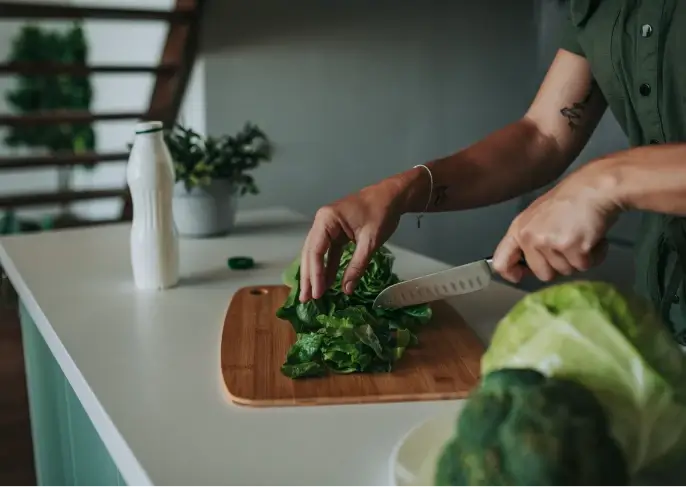 A man chopping spinach or kale with knife and the head of broccoli and cabbage on a plate at the side.